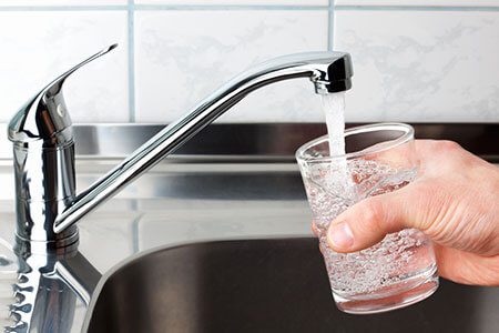 Water being poured from a faucet into a clear glass.