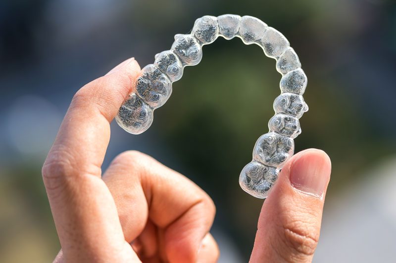 Person holding a plastic aligner in their hand.