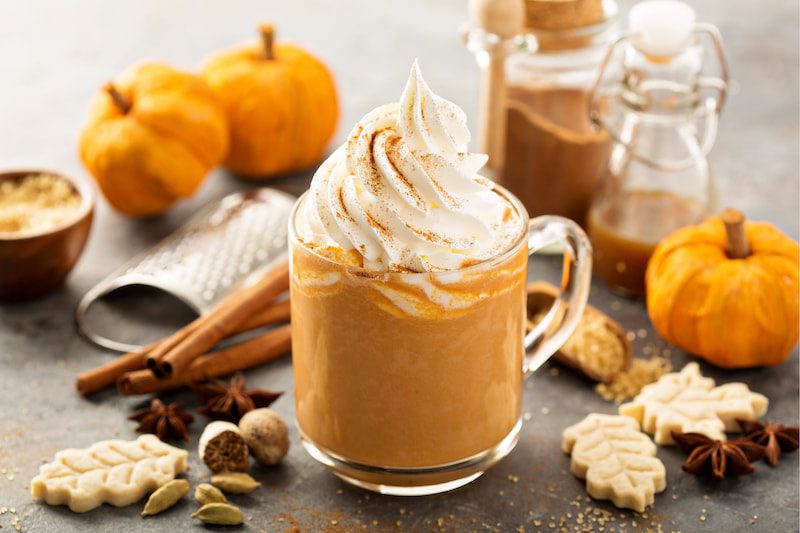 Pumpkin spice latte in a glass mug with cinnamon, nutmeg and cookies