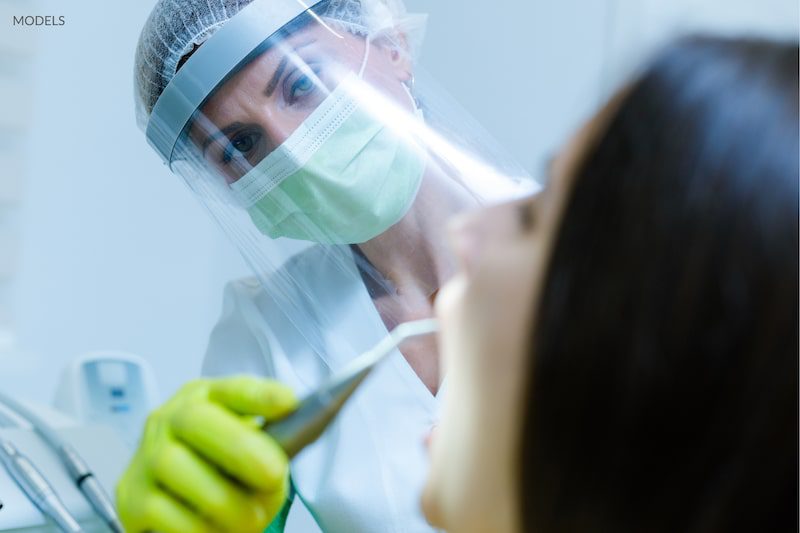 Dental hygienist cleaning a patients teeth while wearing PPE to protect from COVID