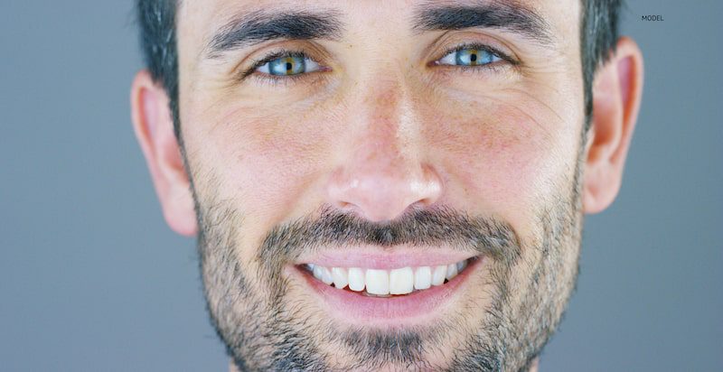 Man smiling in front of a blue-gray background.